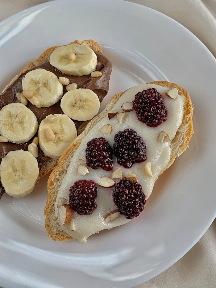Close-up of toasted bread with bananas and blackberries on ceramic plate.